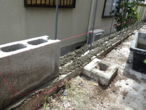 モルタルを入れ、コンクリートブロックを置いていきます。 最初にブロックを設置する部分の端と端にブロックを置き、糸を張っていきます。 この作業がかなり重要で一直線・水平を正確に積むための基準を作ります。